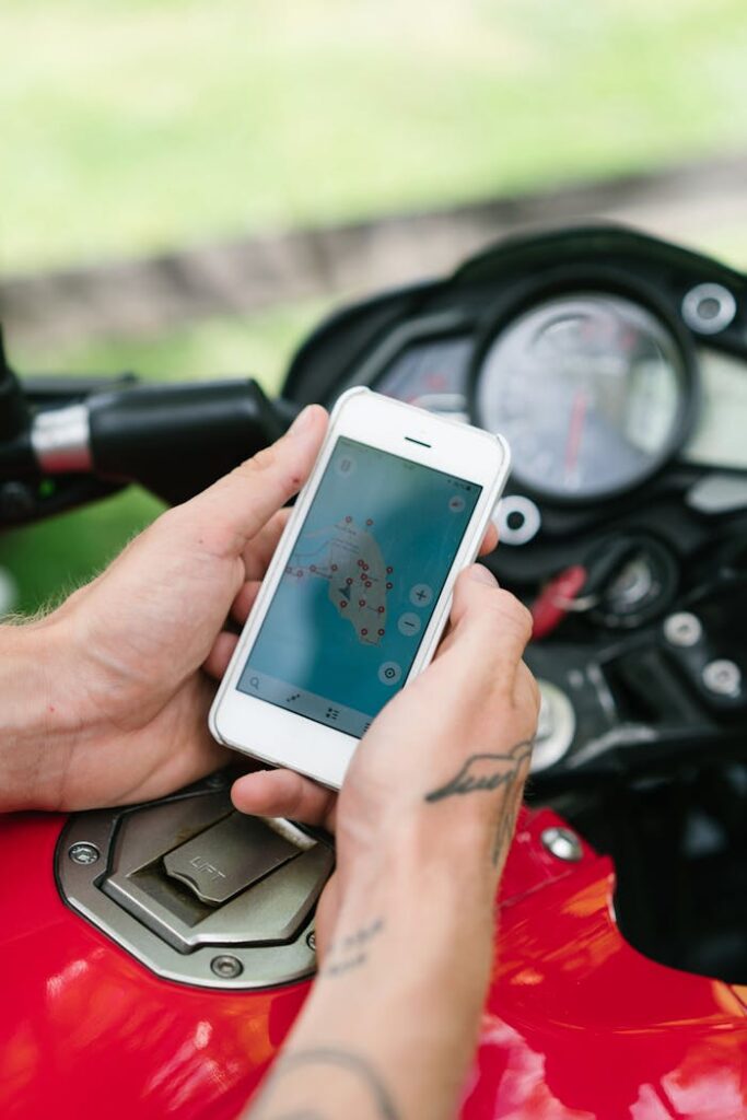 From above of crop anonymous tattooed male holding smartphone while studying map of island via Internet sitting on motorbike on street